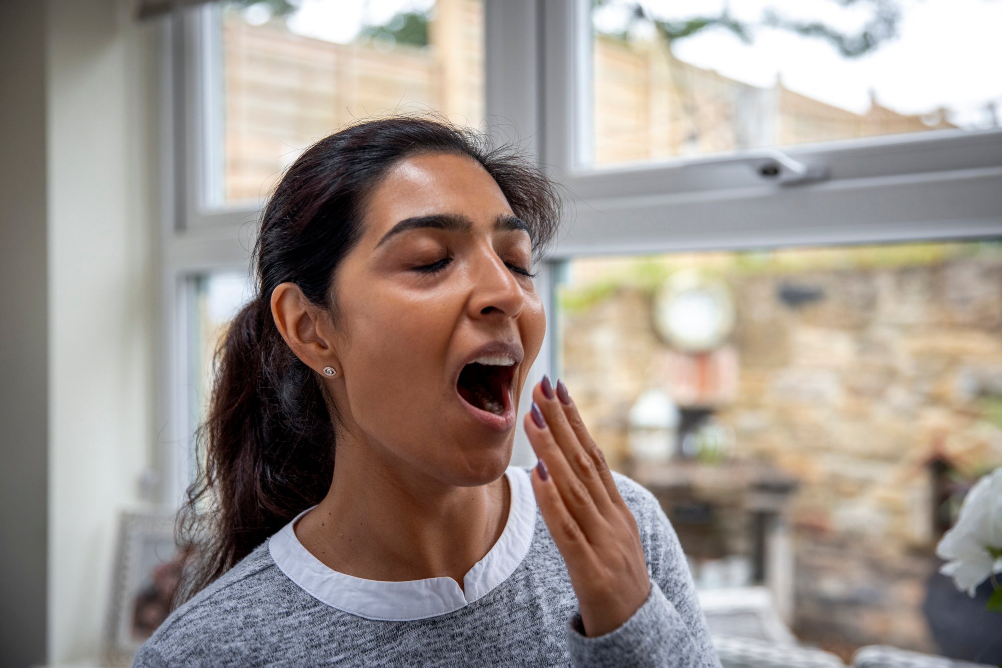 Person experiencing daytime fatigue and yawning at home.